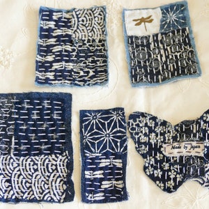 May include: Five blue and white fabric squares with different patterns, including a dragonfly, flowers, and geometric designs. The squares are stitched together and have a label that reads "Made by Japan".