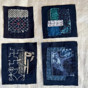 May include: Four square fabric patches featuring dark blue indigo-dyed textiles with various white and teal geometric patterns, sashiko-style stitching, and a small white label with the handwritten text "CIRCLE: BLUE" on one of the patches.