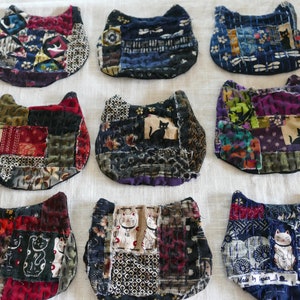 May include: Nine handmade patchwork cat-shaped coasters with various patterns and colors, including black, red, white, and blue. Some coasters feature a cat silhouette.