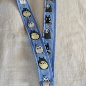 May include: A blue lanyard with a white and black pattern featuring cartoon characters. The lanyard has a silver metal clip.