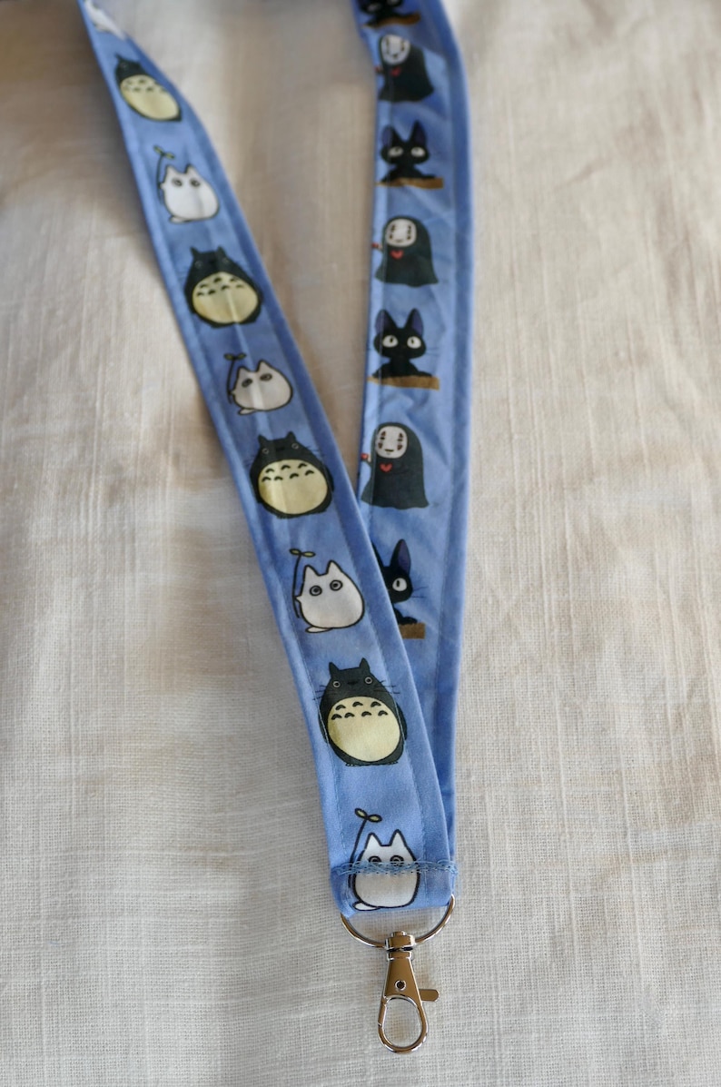 May include: A blue lanyard with a white and black pattern featuring cartoon characters. The lanyard has a silver metal clip.