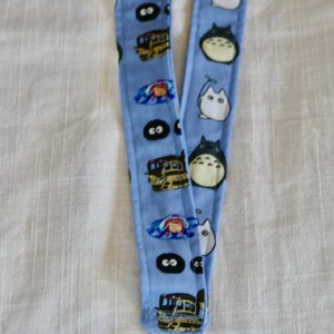 May include: A blue lanyard with a white clip. One side features a repeating pattern of Totoro and Catbus characters from the movie My Neighbor Totoro. The other side features a repeating pattern of No Face characters from the movie Spirited Away.