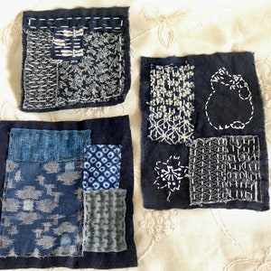 May include: Four blue and white fabric squares with different patterns and stitching. The squares are sewn together to create a larger square.
