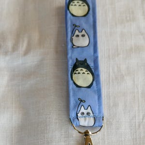 May include: A blue key chain with a silver clip. The key chain has a repeating pattern of white and black cartoon characters.