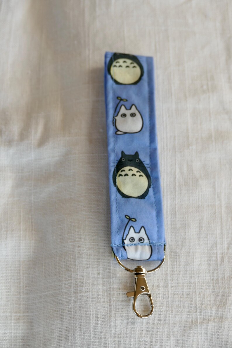 May include: A blue key chain with a silver clip. The key chain has a repeating pattern of white and black cartoon characters.