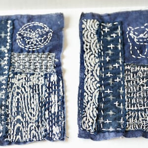 May include: Two blue fabric squares with white stitching in various patterns. The squares are made of patchwork fabric and have a variety of stitching designs, including cross-stitching, running stitch, and back stitch.