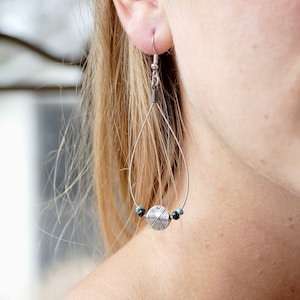 May include: Silver teardrop earrings with a geometric patterned charm and turquoise and black beads.