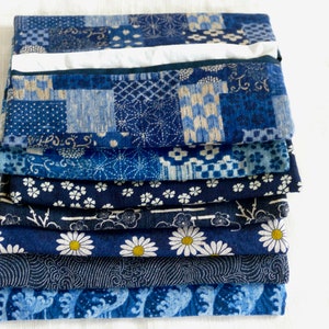 May include: A stack of eight blue fabric squares with different patterns, including geometric designs, flowers, and waves. The fabric is a traditional Japanese indigo dye.