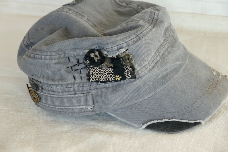 Peut inclure: Une casquette en toile grise &agrave; l'aspect us&eacute;. La casquette a un patch cousu sur le devant avec un motif g&eacute;om&eacute;trique noir et blanc. La casquette a un petit bouton m&eacute;tallique sur le c&ocirc;t&eacute;.