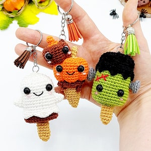 Op de afbeelding: Drie gehaakte Halloween-ijs-sleutelhangers. De hangers zijn een geest, een pompoen en een Frankenstein-monster. Elke hanger heeft een schattig gezicht en is bevestigd aan een zilveren sleutelhanger met een kwast.