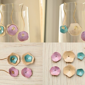 Peut inclure: Un ensemble de six boucles d'oreilles faites à la main avec des breloques en métal en forme de fleur dans des tons de turquoise, rose et crème. Les breloques sont attachées à des crochets d'oreilles en fil de fer doré.