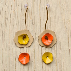Peut inclure: Une paire de boucles d'oreilles avec un motif de fleur beige, jaune et orange. Les boucles d'oreilles sont en métal et ont un fil long et incurvé.