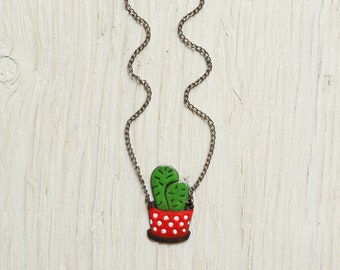 May include: A silver chain necklace with a green cactus plant in a red pot with white polka dots.