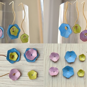 Peut inclure: Une paire de boucles d'oreilles faites à la main avec des formes de fleurs superposées en émail bleu, vert et violet. Les boucles d'oreilles sont faites de fil et ont un design suspendu.
