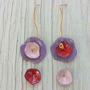 Peut inclure: Boucles d'oreilles florales faites à la main avec un fil doré et un design superposé. Les boucles d'oreilles présentent une couche extérieure violette, une couche intérieure rose ou rouge et un tourbillon doré au centre.