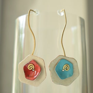 Peut inclure: Une paire de boucles d'oreilles avec un motif de fleur blanc, rouge et bleu. Les boucles d'oreilles sont en métal et ont une boucle de fil dorée.