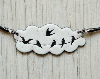 Könnte beinhalten: Eine weiße Keramik-Halskette mit einem Wolkenanhänger und schwarzen Silhouetten von Vögeln, die auf einem Draht sitzen. Die Halskette hat eine schwarze Lederkordel.