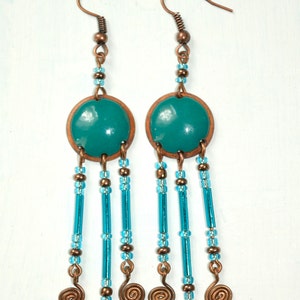 May include: Teal blue and copper dangle earrings with a round teal blue charm and multiple strands of blue beads and copper wire spirals.