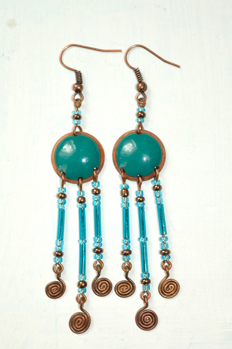 May include: Teal blue and copper dangle earrings with a round teal blue charm and multiple strands of blue beads and copper wire spirals.