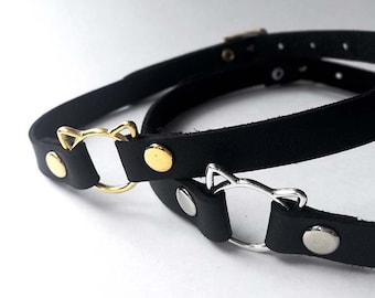 May include: Two black leather choker necklaces with metal cat head charms. One charm is gold and the other is silver.
