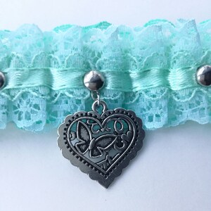 May include: A light blue lace choker with a silver heart charm featuring a butterfly design.