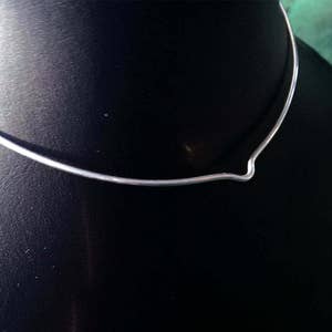 May include: A silver choker necklace with a V-shaped design. The necklace is on a black background.