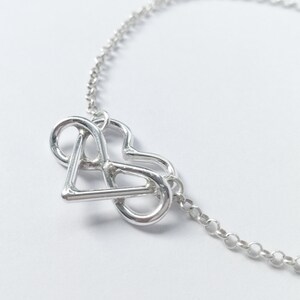 Puede incluir: Un collar de plata con un colgante que presenta un símbolo de infinito entrelazado con un corazón.