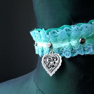 May include: A turquoise and white lace choker with a silver heart charm. The choker has silver studs and a white satin ribbon.