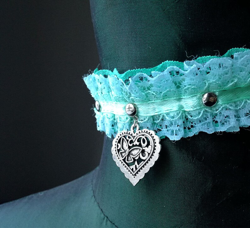 May include: A turquoise and white lace choker with a silver heart charm. The choker has silver studs and a white satin ribbon.