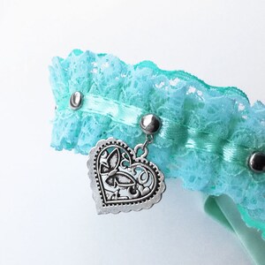 May include: A light blue lace choker with a silver heart charm. The heart charm has a decorative butterfly design.