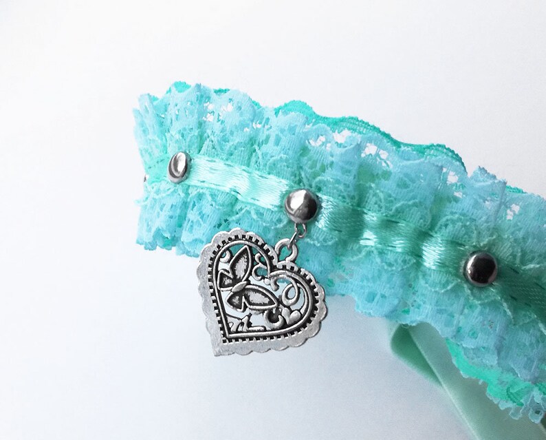May include: A light blue lace choker with a silver heart charm. The heart charm has a decorative butterfly design.