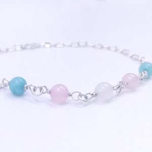 Puede incluir: Un brazalete de cadena de plata con cuentas de color azul claro, rosa y blanco.