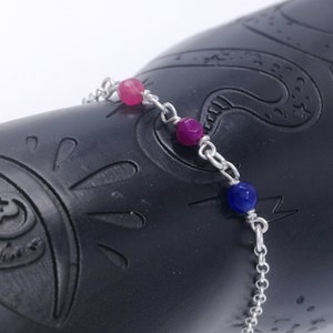 May include: A silver chain bracelet with three gemstone beads: pink, purple, and blue.