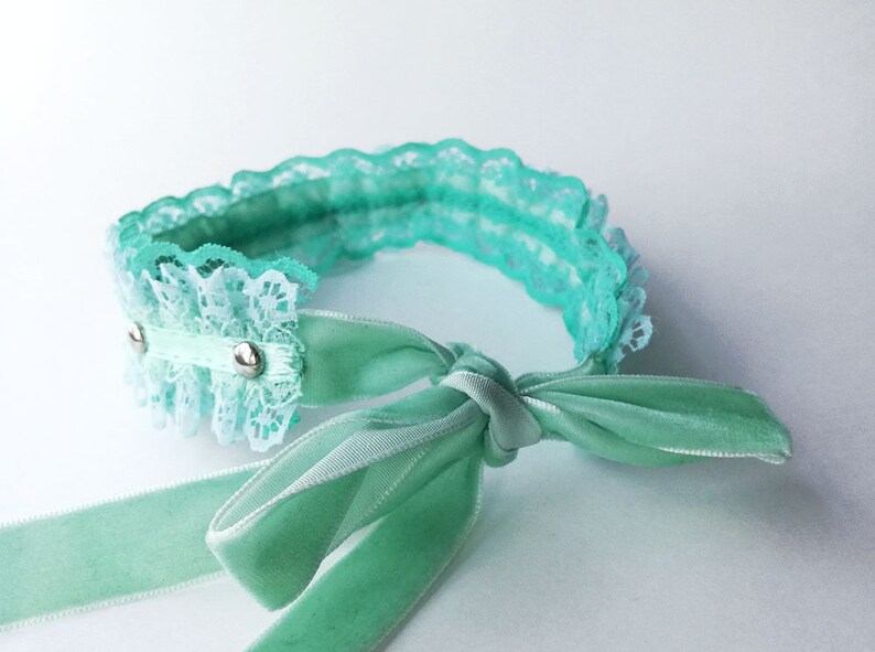 May include: A light green lace choker with a matching satin ribbon tied in a bow. The choker has two silver metal accents.