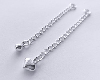 May include: Two silver chains with a small ball at one end and a heart charm at the other end.
