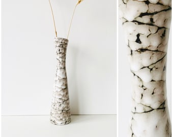 May include: A white ceramic vase with a crackled glaze pattern. The vase has a narrow neck and a wide base. It is decorated with brown and black lines.