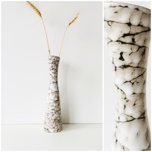 Op de afbeelding: Een witte keramische vaas met een gekrakelde glazuurpatroon. De vaas heeft een smalle hals en een brede basis. Het is versierd met bruine en zwarte lijnen.