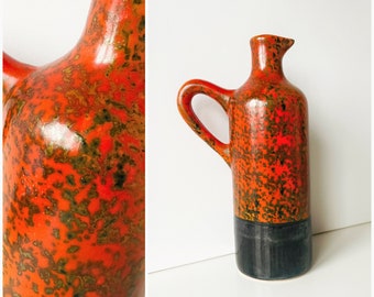Könnte beinhalten: Hoher Keramik-Krug mit Henkel und Ausguss. Der Krug hat eine gesprenkelte orangefarbene und braune Glasur im oberen Bereich und einen schwarzen Sockel. Das Design ist im Vintage-Stil.