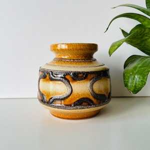 May include: A ceramic vase with a rounded body and a narrow neck. The vase features a pattern of brown and black organic shapes against a cream background. The top and bottom rims are brown. The vase is a decorative item.