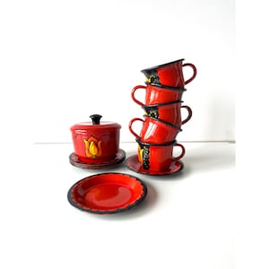 May include: A set of red and black enamel teacups and saucers with a floral design. The set includes a sugar bowl with a matching design.