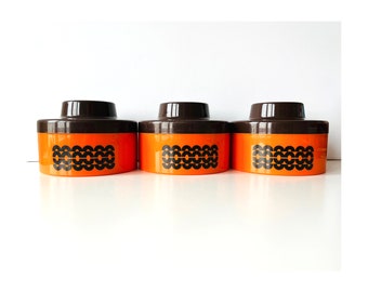 Könnte beinhalten: Set aus drei orangefarbenen und braunen Keramikbehältern mit geometrischem Muster. Die Behälter haben einen Deckel und sind perfekt zum Aufbewahren von Küchenutensilien.