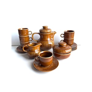 May include: A vintage brown ceramic tea set, including a teapot, creamer, sugar bowl, cups, and saucers. The set has a ribbed design and is arranged on a white surface. The cups are stacked in pairs, and the set appears to be complete.