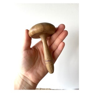 May include: A wooden mushroom-shaped tool with a brown finish. The tool has a smooth, rounded top and a long, slender stem.