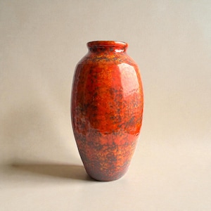 Può includere: Un vaso in ceramica alto e lucido con un motivo maculato e screziato nei toni del rosso, arancione e marrone scuro. Il vaso ha un corpo arrotondato e un bordo leggermente svasato.