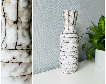 May include: White ceramic vase with a textured, striped design. The vase has a narrow neck and a wide base.