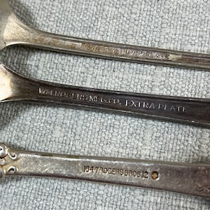May include: Three silver-plated spoons with engraved markings on the handles. The top handle reads EMBASSY SILVER PLATE, the middle reads WM. ROGERS MFG. CO. EXTRA PLATE, and the bottom handle reads 1847 ROGERS BROS. 12 with a small circular icon.