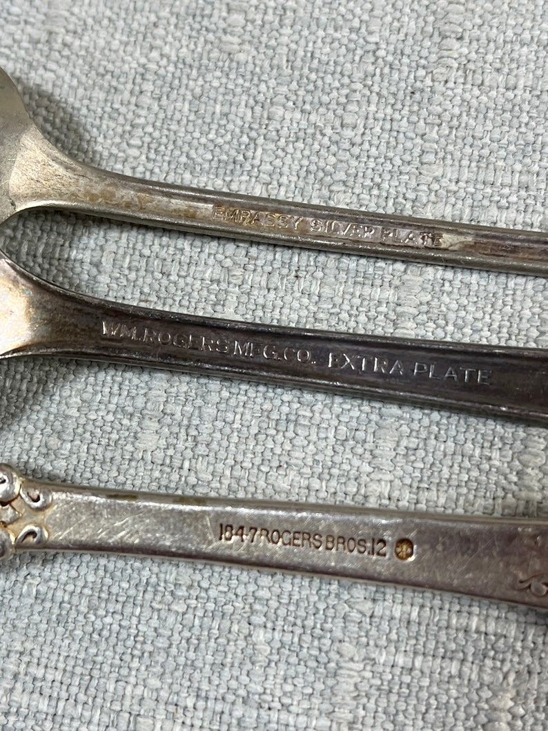May include: Three silver-plated spoons with engraved markings on the handles. The top handle reads EMBASSY SILVER PLATE, the middle reads WM. ROGERS MFG. CO. EXTRA PLATE, and the bottom handle reads 1847 ROGERS BROS. 12 with a small circular icon.