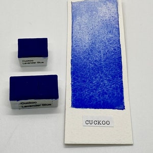 May include: Two watercolor paint pans labeled "Cuckoo Lavender Blue" with a blue watercolor swatch on a white card labeled "CUCKOO".