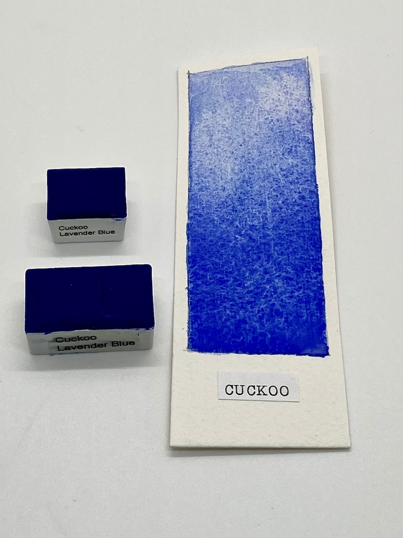 May include: Two watercolor paint pans labeled "Cuckoo Lavender Blue" with a blue watercolor swatch on a white card labeled "CUCKOO".
