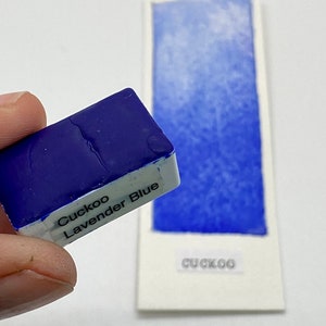 May include: A small, blue watercolor paint pan labeled "Cuckoo Lavender Blue".